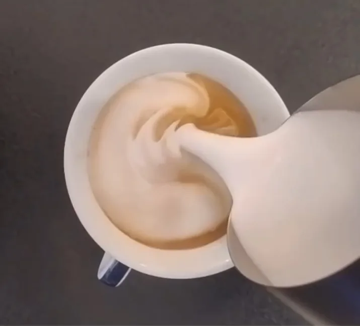 Un cappuccino con la foglia disegnata nella schiuma, mentre viene versato il latte