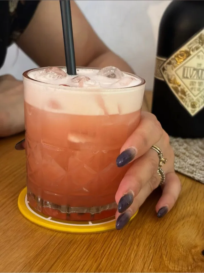 Un cocktail rosa con la schiuma, tenuto in mano su un tavolo di legno
