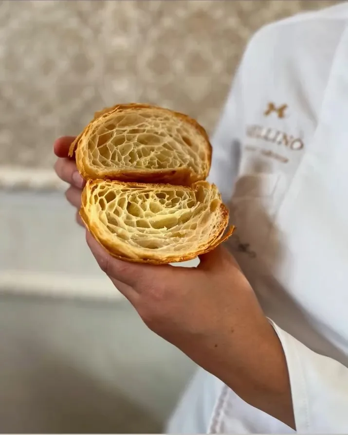 Un cornetto sfogliato aperto a meta', tenuto in mano, con la sfoglia a nido d'ape ben visibile