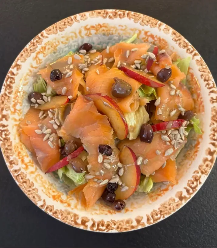 Una grande insalata con salmone affumicato, pesca, semi e foglie, servita in una scodella gialla