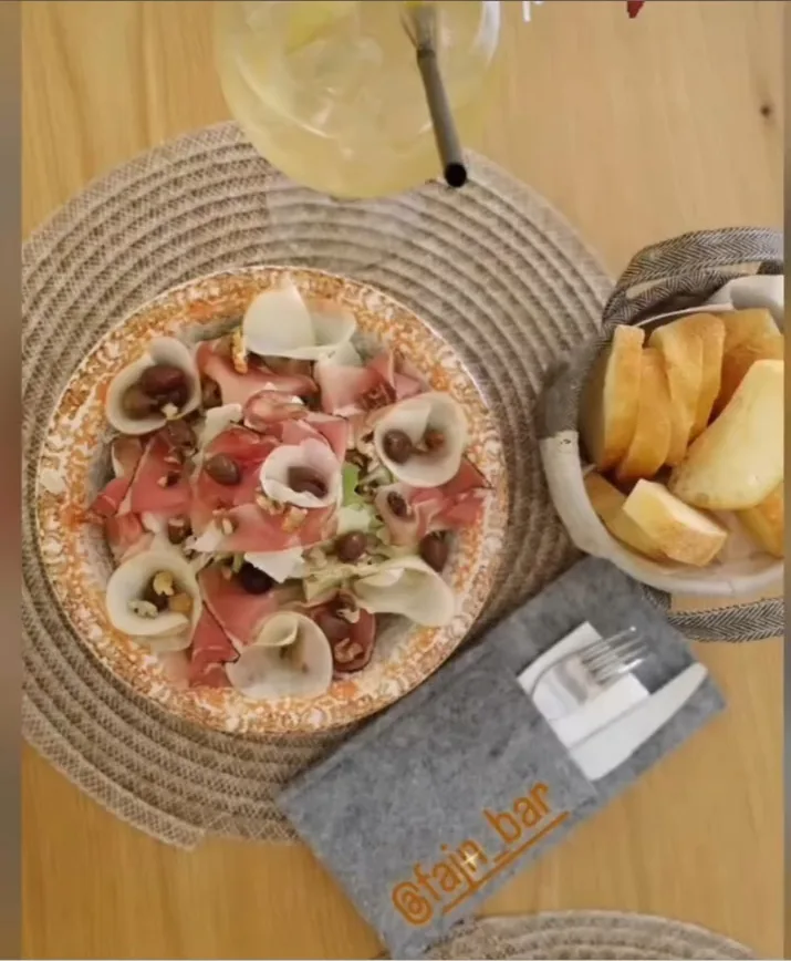 Una pinsa con prosciutto crudo e mozzarella su un piatto tondo, con il pane e le posate accanto