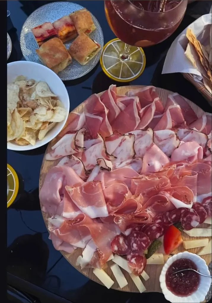 Un tagliere di salumi e formaggi visto dall'alto, con due cocktail, il pane e le salse attorno