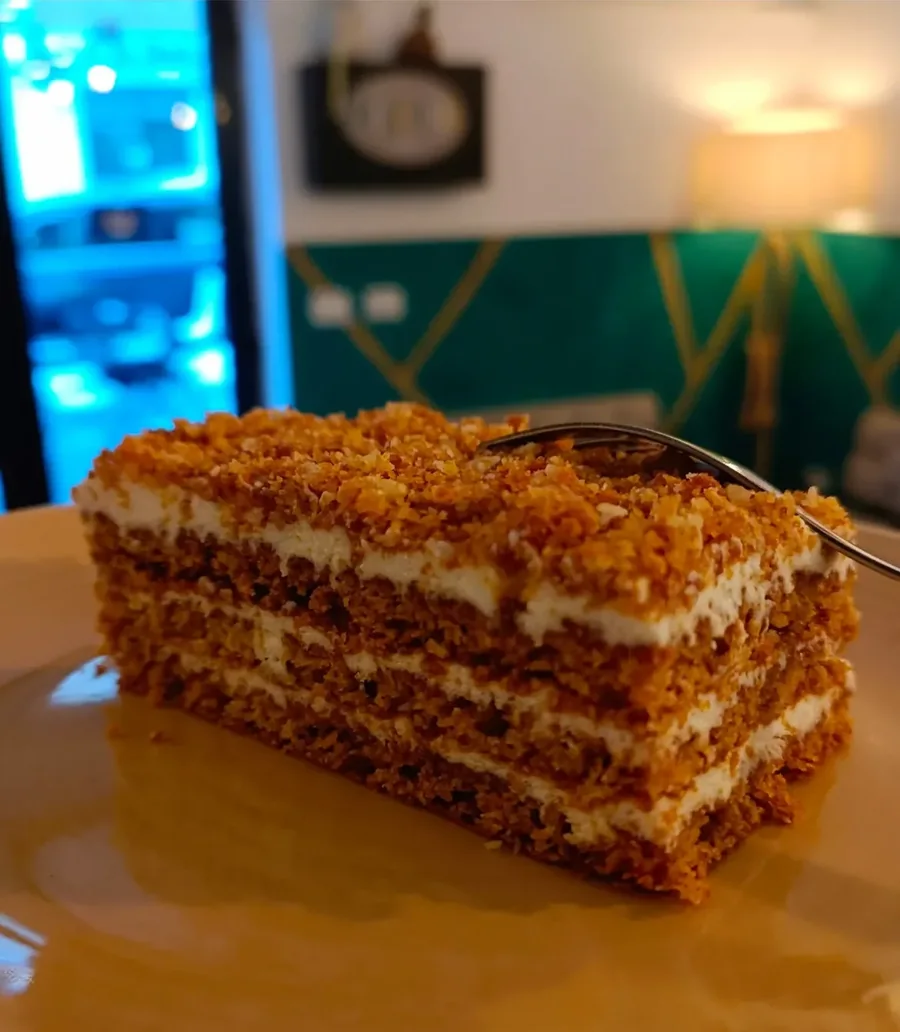 Una fetta di torta slovacca a strati, con la crema chiara fra gli strati e la granella di noci sopra, servita su un piatto
