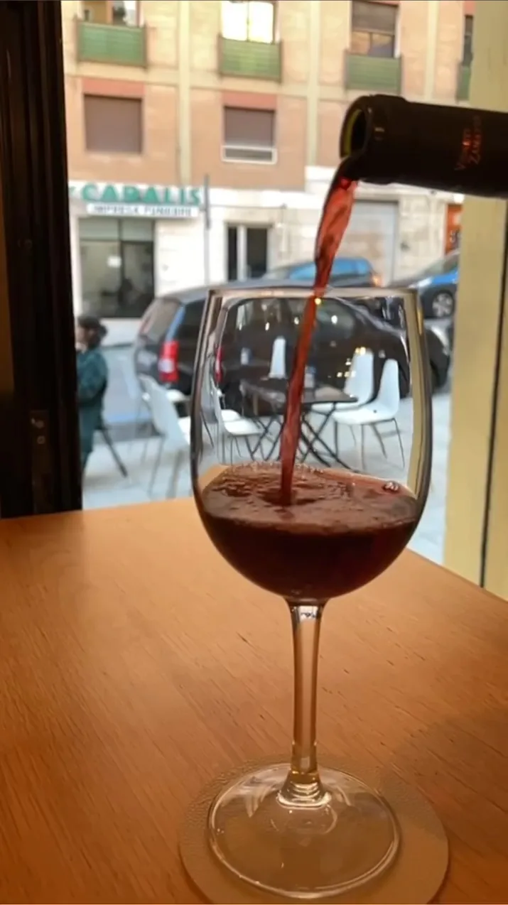Un calice di vino rosso mentre viene versato, con la strada e i palazzi sullo sfondo